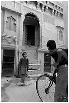 Boy on bicycle looking at girl in front of blue house. Jodhpur, Rajasthan, India (black and white)