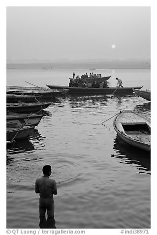 Man standing in Ganga River and boats at sunrise. Varanasi, Uttar Pradesh, India (black and white)