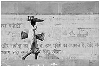 Man carrying a plater in front of wall with inscriptions in Hindi. Varanasi, Uttar Pradesh, India ( black and white)