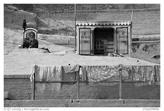 Sadhu sitting next to shrine and laundry. Varanasi, Uttar Pradesh, India