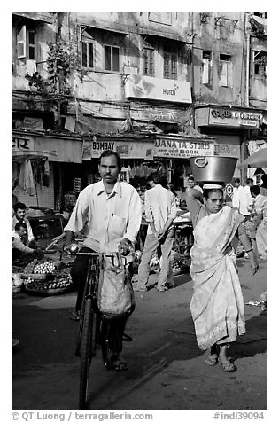 Man riding bike and woman with basket on head, Colaba Market. Mumbai, Maharashtra, India