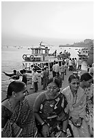 Women sitting on waterfront with boats behind at twilight. Mumbai, Maharashtra, India ( black and white)