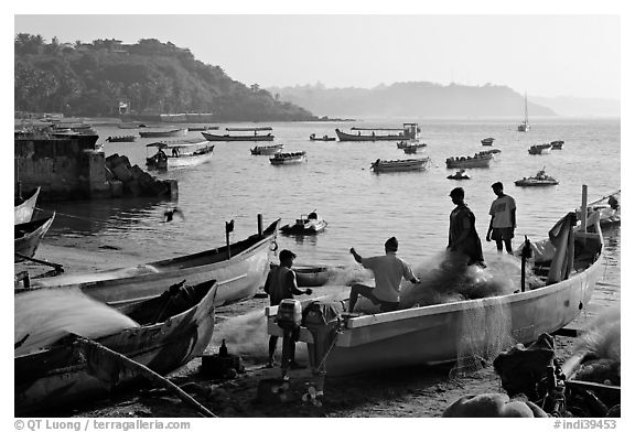 Men repairing net in small fishing boat, early morning, Dona Paula. Goa, India (black and white)