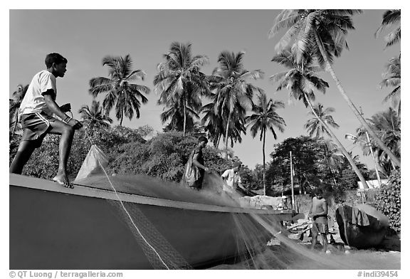 Men mending fishing net with palm trees in background. Goa, India (black and white)