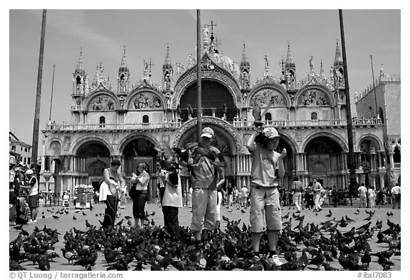 Children feeding flock of pigeon, in front of the Basilica San Marco, mid-day. Venice, Veneto, Italy (black and white)