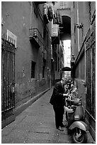 Man locking his motorbike in a side street. Naples, Campania, Italy (black and white)