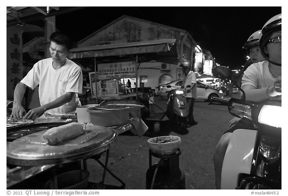 Man preparing food as people wait on motorbike. George Town, Penang, Malaysia