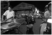 Man preparing food as people wait on motorbike. George Town, Penang, Malaysia ( black and white)