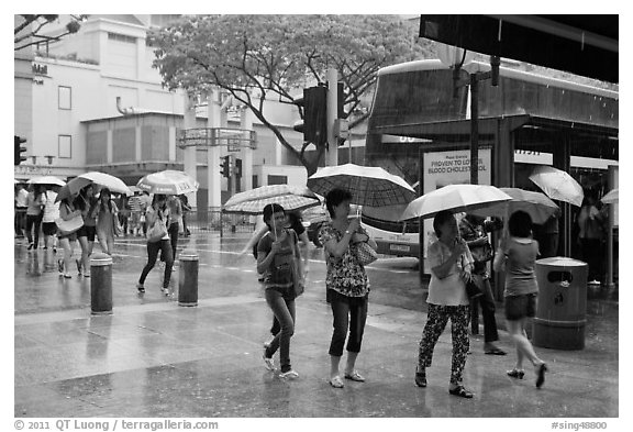 Women cross street of shopping area during shower. Singapore