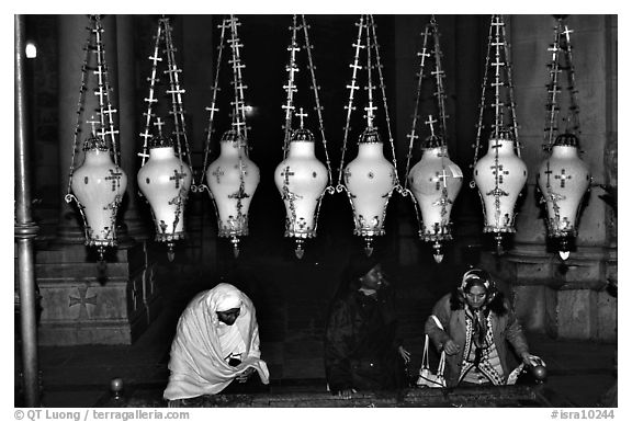 Women worshiping beneath hanging lamps inside the Church of the Holy Sepulchre. Jerusalem, Israel (black and white)