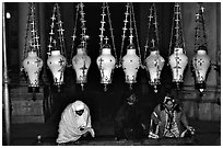 Women worshiping beneath hanging lamps inside the Church of the Holy Sepulchre. Jerusalem, Israel (black and white)