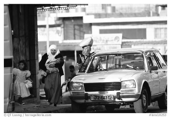 Women next to an old French Peugeot car, Hebron. West Bank, Occupied Territories (Israel) (black and white)
