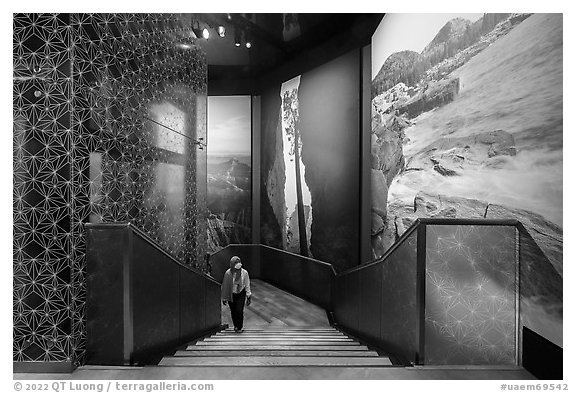 Visitor walking up stairs looking at mural prints, USA Pavilion. Expo 2020, Dubai, United Arab Emirates (black and white)