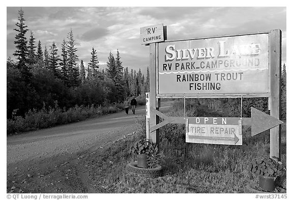 Sign and couple walking on McCarthy road near Silver Lake. Wrangell-St Elias National Park, Alaska, USA.
