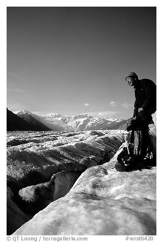 Hiker reaches for item in backpack on Root Glacier. Wrangell-St Elias National Park, Alaska, USA.