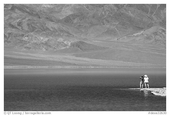 Two tourists on shore of rare lake on the floor of the Valley. Death Valley National Park, California, USA.