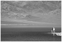 Two tourists on shore of rare lake on the floor of the Valley. Death Valley National Park, California, USA. (black and white)