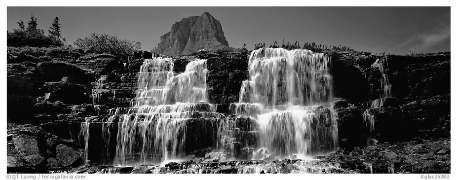 Waterfall flowing over dark rock and peak. Glacier National Park (black and white)