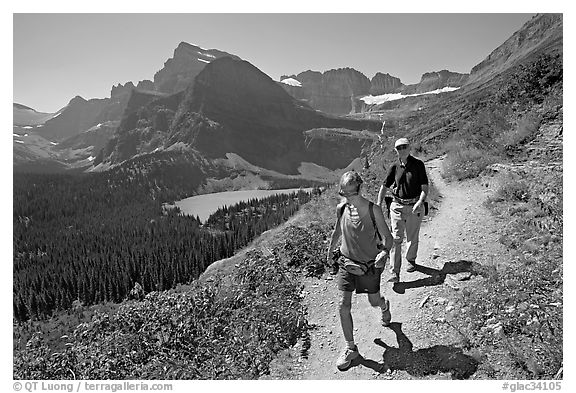 Couple hiking on trail, with Grinnell Lake below. Glacier National Park, Montana, USA.