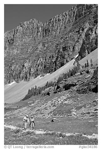 Couple hiking on trail amongst wildflowers near Hidden Lake. Glacier National Park, Montana, USA.