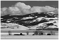 Distant row of barns, hills and clouds in winter. Grand Teton National Park, Wyoming, USA. (black and white)