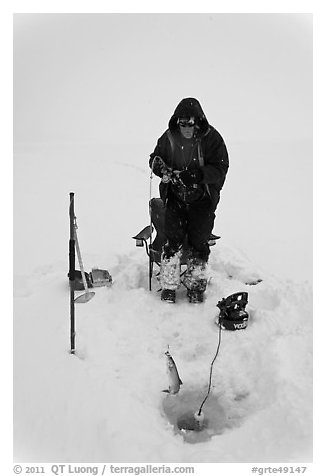 Man catching fish through hole in Jackson Lake ice. Grand Teton National Park (black and white)