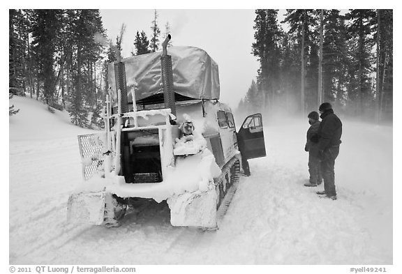 Couple standing in snowdrift next to snow coach. Yellowstone National Park, Wyoming, USA.