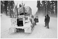 Couple standing in snowdrift next to snow coach. Yellowstone National Park, Wyoming, USA. (black and white)
