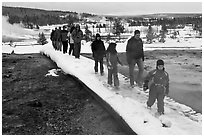 Tourists walk over snow-covered boardwalk. Yellowstone National Park, Wyoming, USA. (black and white)
