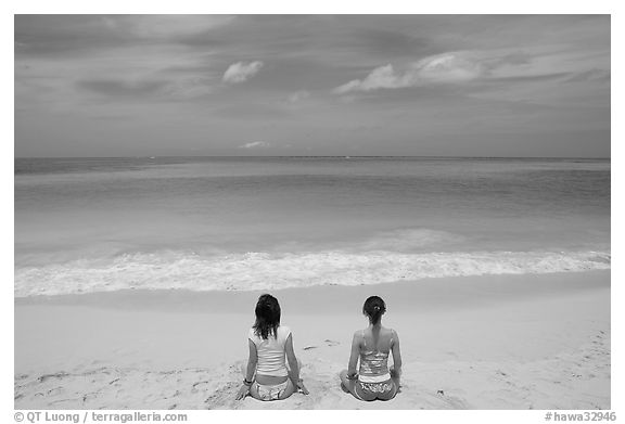 Young women facing ocean in meditative pose on Waimanalo Beach. Oahu island, Hawaii, USA (black and white)