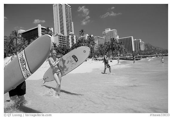 Women carrying surfboards into the water, Waikiki Beach. Waikiki, Honolulu, Oahu island, Hawaii, USA (black and white)