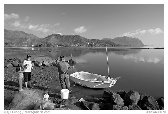 Fisherman and family pulling out net out of small baot, Kaneohe Bay, morning. Oahu island, Hawaii, USA (black and white)