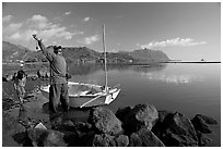 Fisherman pulling out fish out a net, with girl looking, Kaneohe Bay, morning. Oahu island, Hawaii, USA (black and white)