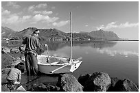 Fisherman pulling out fish out a net as girllooks, Kaneohe Bay, morning. Oahu island, Hawaii, USA ( black and white)