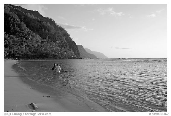 Couple standing in water looking at the Na Pali Coast, Kee Beach, late afternoon. Kauai island, Hawaii, USA (black and white)