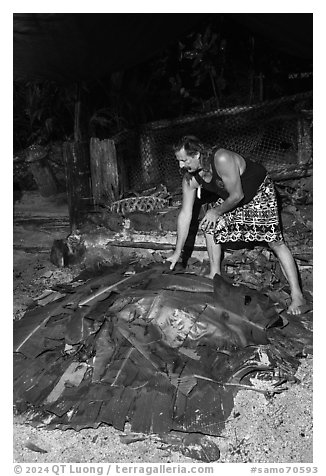 Candy Mann taking out banana leaves to uncover Umu earth oven, Tisa Barefoot Bar. Tutuila, American Samoa (black and white)