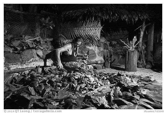 Man retrieving food cooked in Samoan traditional cooking oven powered by hot rocks. Tutuila, American Samoa (black and white)