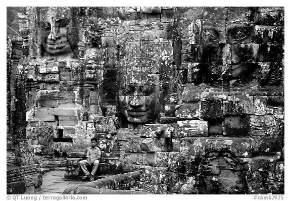 Boy sits next to large stone smiling faces, the Bayon. Angkor, Cambodia (black and white)