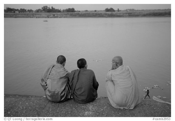 Buddhist monks sit on  banks of Tongle Sap river at dusk,  Phnom Phen. Cambodia