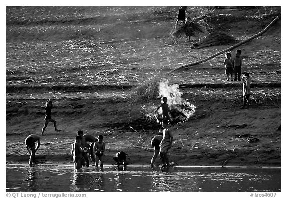 Children bathe in the river and dry out near a fire in a small hamlet. Mekong river, Laos