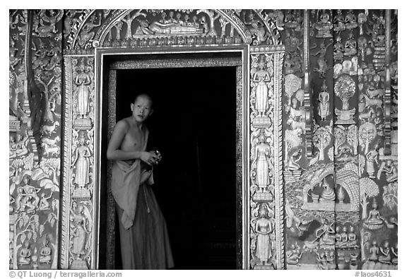 Buddhist novice monk stands at door of shrine, Wat Xieng Thong. Luang Prabang, Laos (black and white)