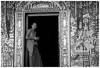 Buddhist novice monk stands at door of shrine, Wat Xieng Thong. Luang Prabang, Laos ( black and white)