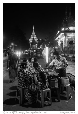 Women eating at street stall at night with Shwedagon Pagoda in background. Yangon, Myanmar (black and white)