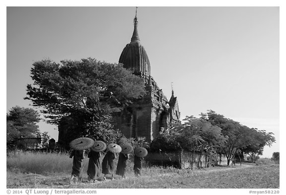 Five novices with red umbrellas walking below temple. Bagan, Myanmar (black and white)