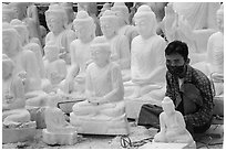 Man working amongst many  buddha statues on Marble street workshop. Mandalay, Myanmar ( black and white)