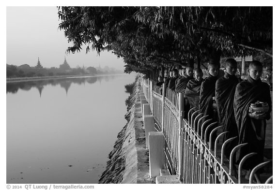 Monks walking in line in alm bowls near Mandalay Fort moat. Mandalay, Myanmar (black and white)