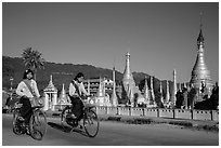 Schoolgirls riding bicycles past golden stupas. Pindaya, Myanmar ( black and white)