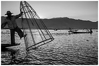 Intha fisherman standing on boat stern to lift net basket. Inle Lake, Myanmar ( black and white)
