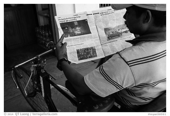 Cyclo driver looking at picture of QT Luong tour group in newspaper. Bago, Myanmar (black and white)