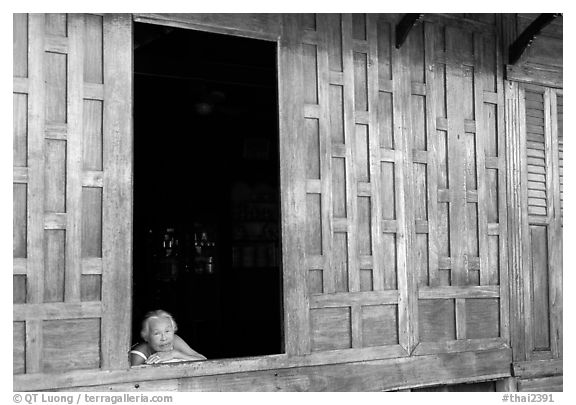 Woman looks out of teak house window. Damonoen Saduak, Thailand